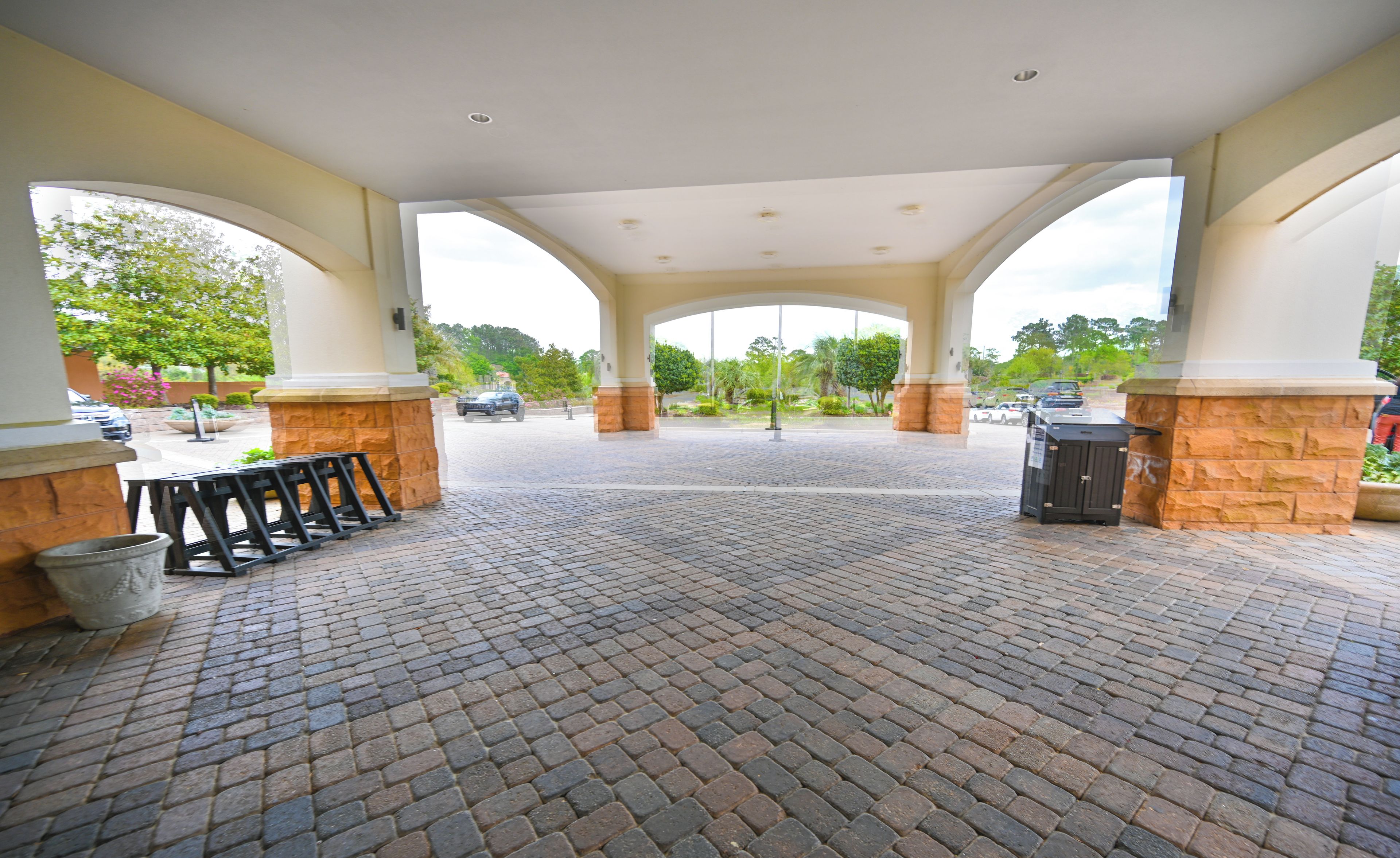 A covered outdoor area with a brick floor, stone pillars, and a view of the parking lot.