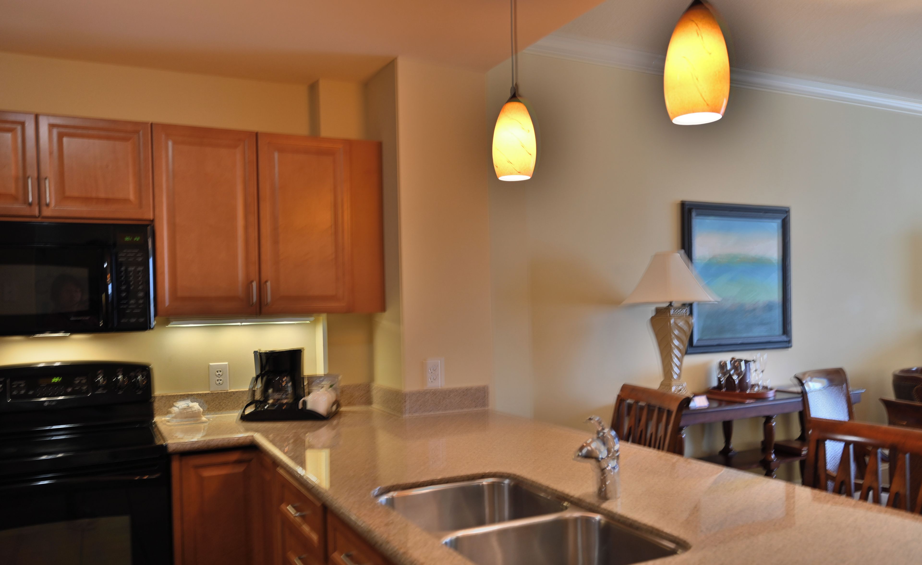 A kitchen with wooden cabinets, a black microwave, a stove, a sink, and pendant lights.
