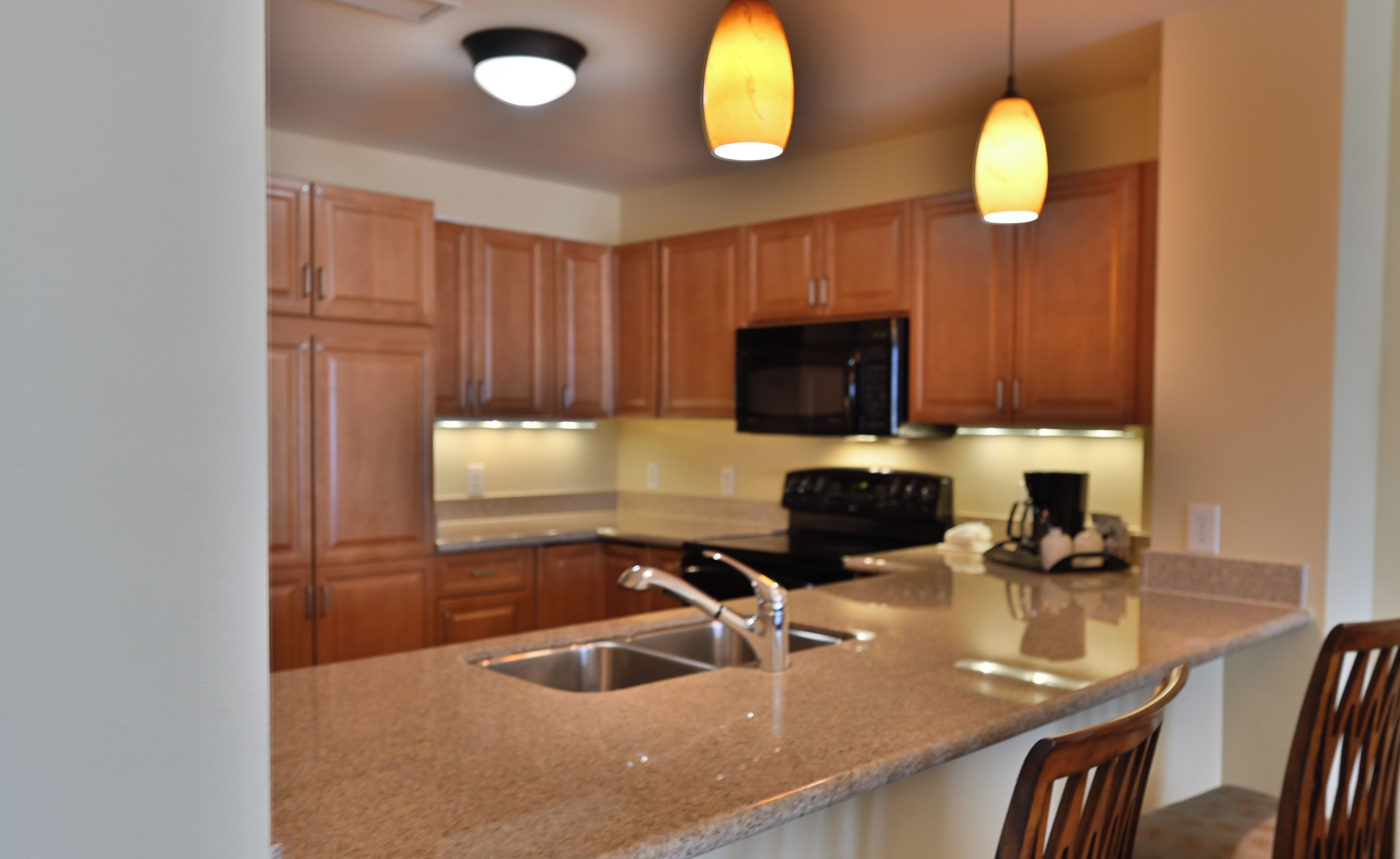 A modern kitchen with wooden cabinets, a granite countertop, stainless steel sink, and a microwave.
