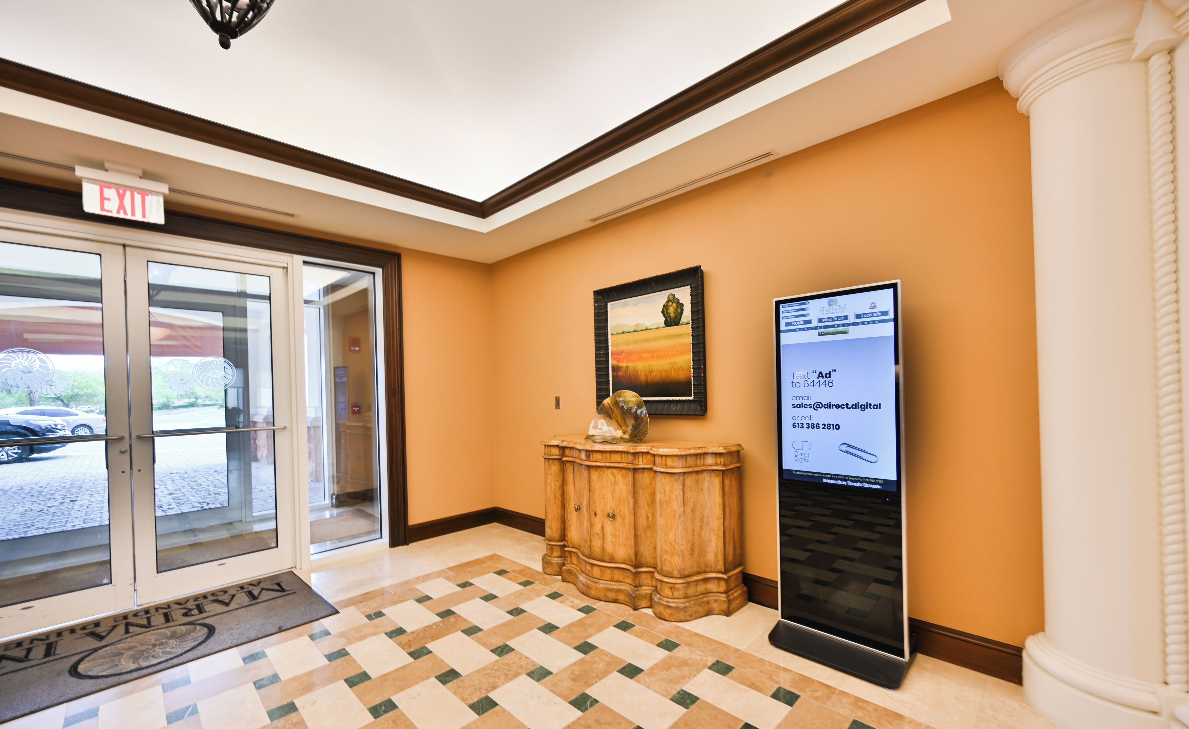 Un vestíbulo de hotel con un mostrador de recepción, una zona de espera y una pantalla digital.