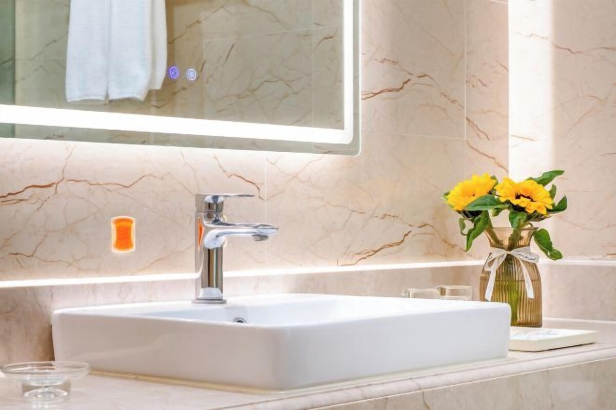 A bathroom with a white sink, a mirror, and a vase with yellow flowers.