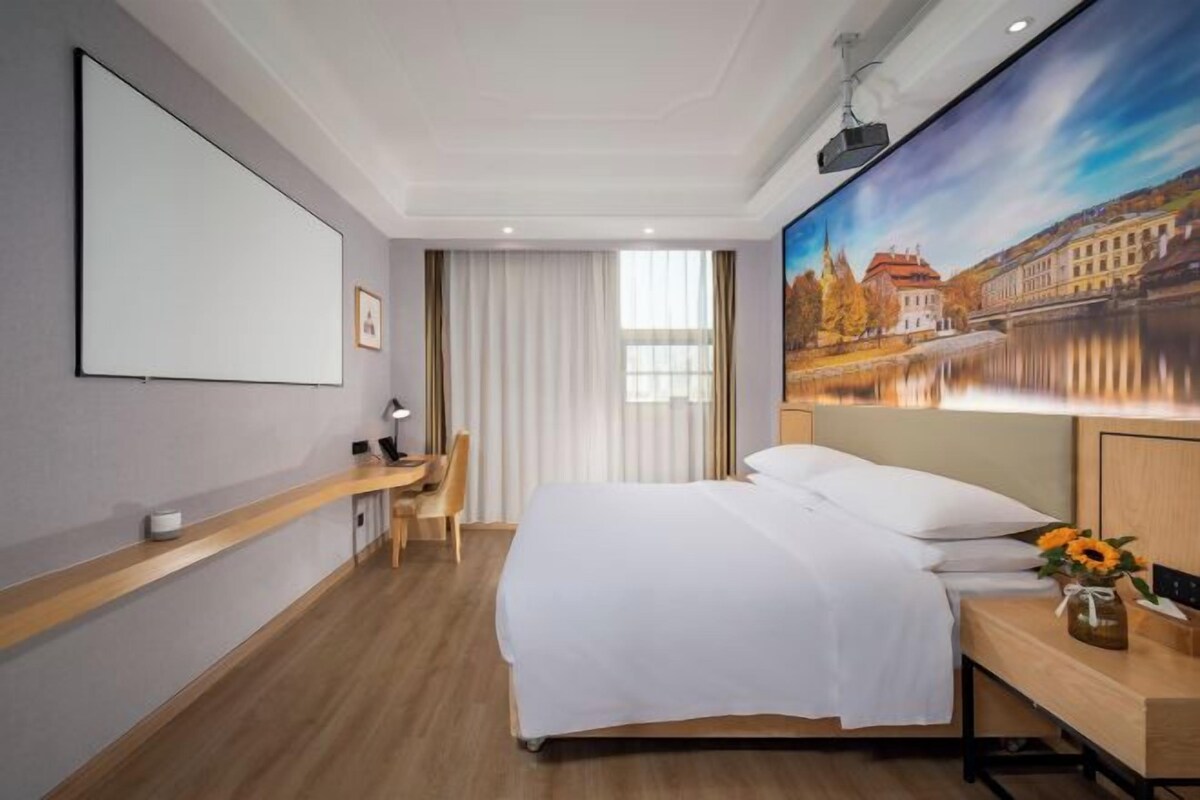 Habitación de hotel con cama, escritorio, silla y un cuadro de un paisaje.