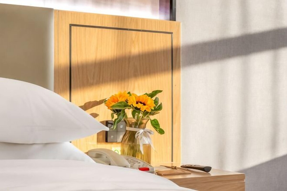 Habitación de hotel con una cama, una mesita de noche con un florero, un teléfono y un panel de pared de madera.