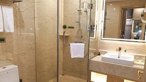 A bathroom with a glass-enclosed shower, a white sink, and a mirror above it. - Vienna Hotel (Rugao)