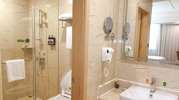 A modern bathroom with a glass-enclosed shower, a toilet, and a sink with a mirror above it. - Vienna Hotel (Rugao)