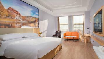 A hotel room with a large bed, a sofa, a desk, and a painting of a building.