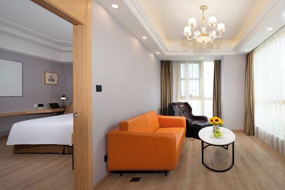 A hotel room with a bed, an orange sofa, a small table with a vase, and a chandelier.