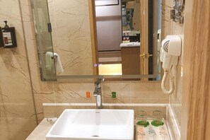 Un baño con lavamanos blanco, cabina de ducha de vidrio y un espejo que refleja un tocador con artículos de aseo.