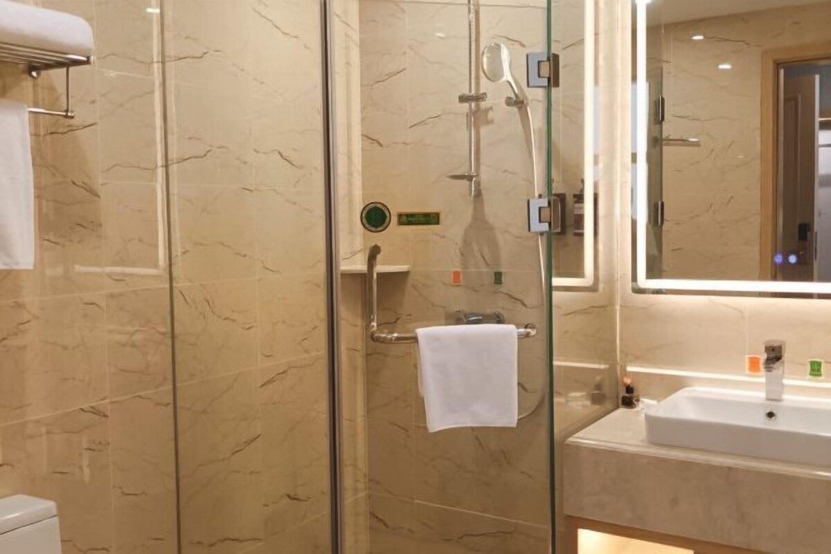 A bathroom with a glass-enclosed shower, a sink with a mirror, and marble walls.