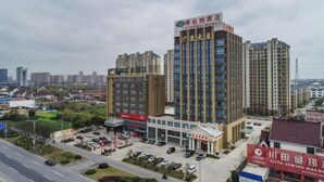 A hotel with multiple floors, a parking lot, and a road in the foreground. - Vienna Hotel (Rugao)