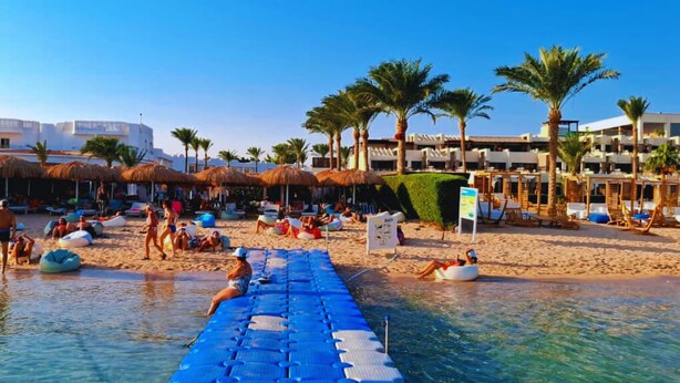 A beach resort with thatched umbrellas, palm trees, and a pool area. - Panoramic Romantic apartment  (South Sinai Governorate)