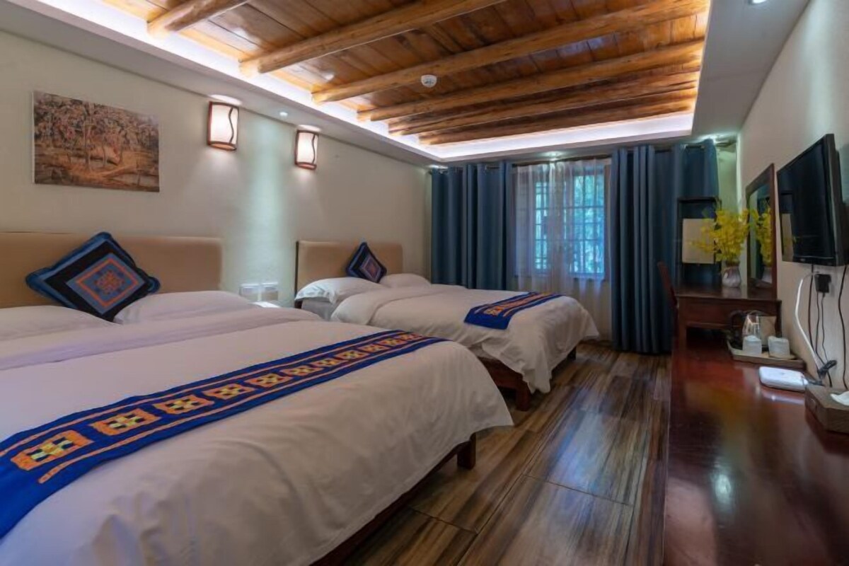 A hotel room with three beds, wooden ceiling beams, a painting on the wall, and a TV on the right side.