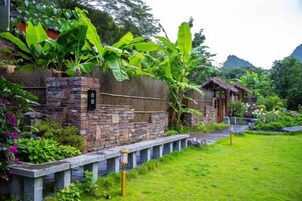 A stone wall with a small structure, lush greenery, and a pathway.