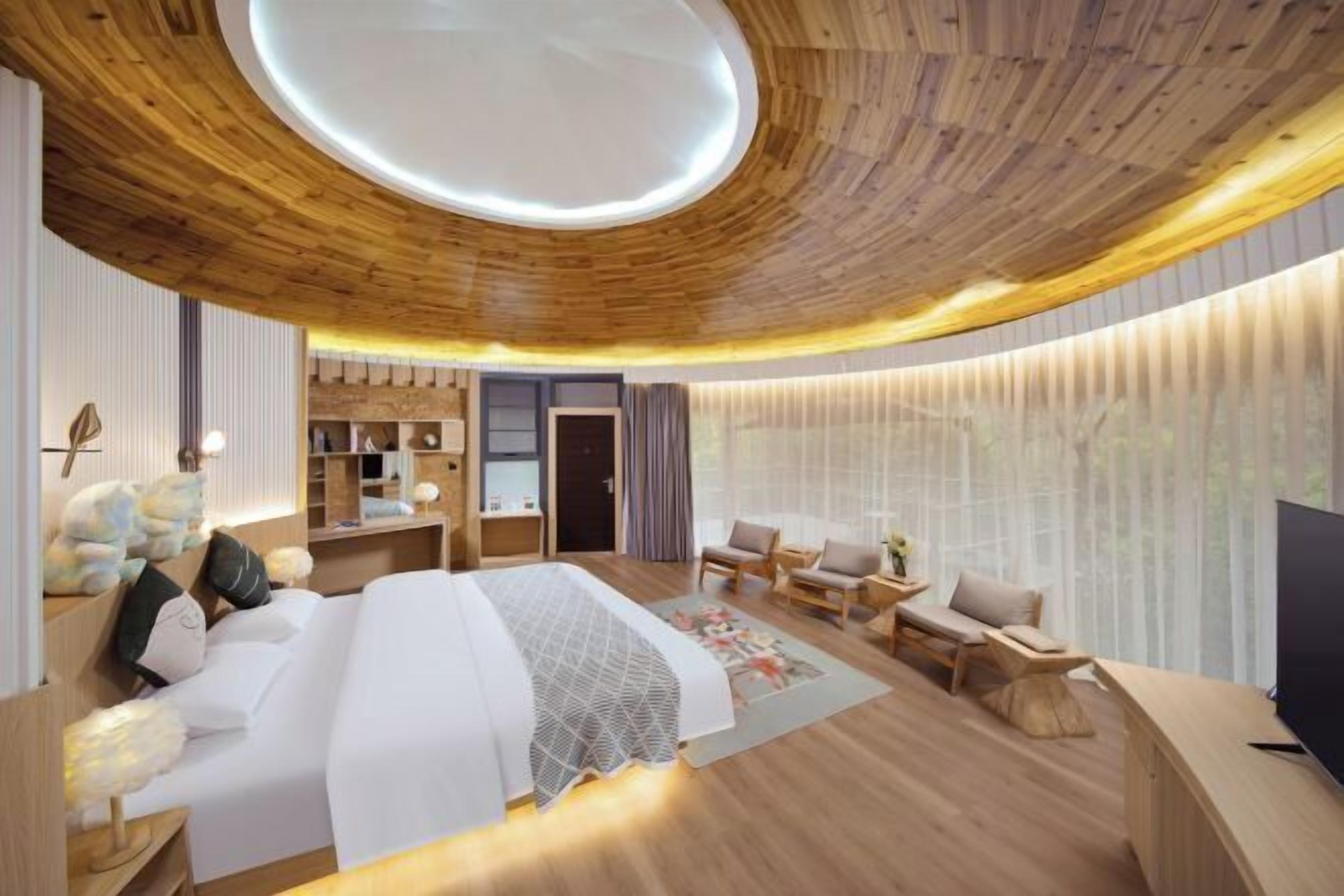 A modern hotel room with a wooden ceiling, a large bed, a desk, and a seating area.