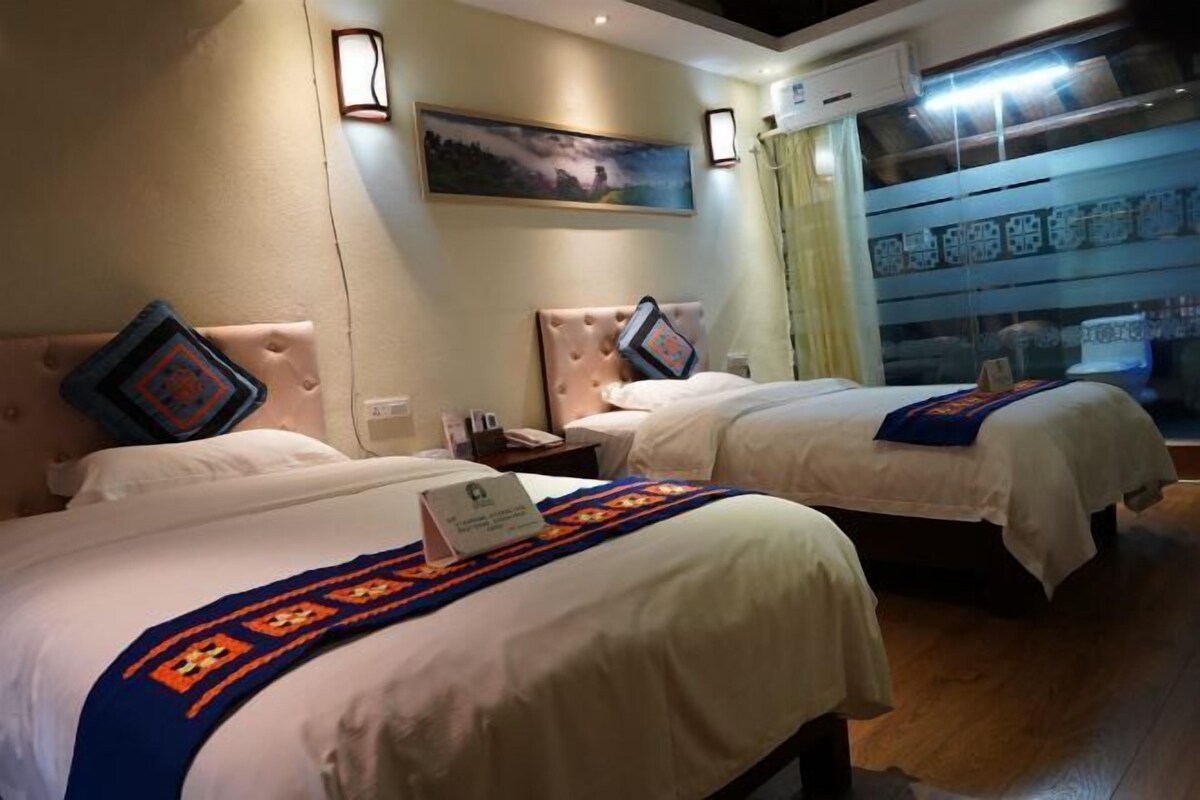 A hotel room with two beds, each with a headboard, a bedside table, a lamp, and a painting on the wall.