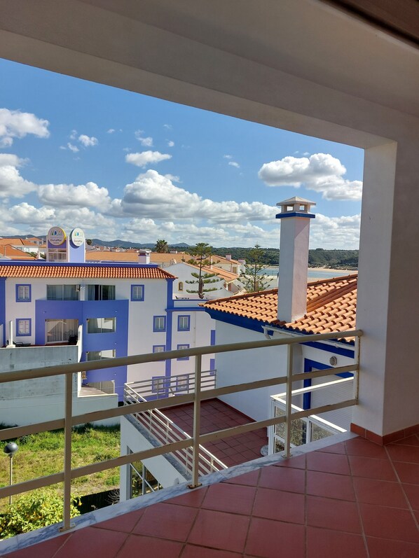 A balcony with a view of a town, including a blue and white building with a sign that reads "DunaMar." - 2-bedroom apartment right on the beach (Vila Nova de Milfontes)