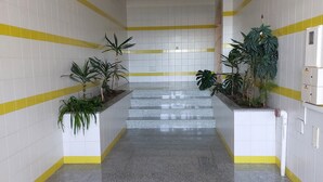 A hallway with white tiled walls, yellow stripes, and granite flooring. There are potted plants on either side of the hallway. - 2 bedrooms beachfront (Vila Nova de Milfontes)