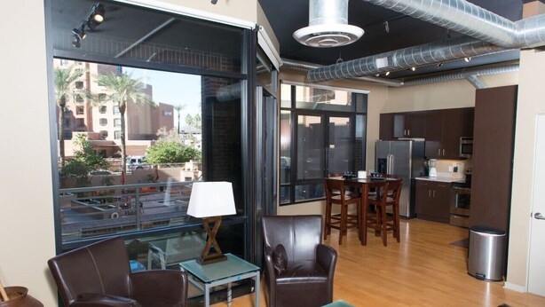 A modern living room with a glass wall, leather furniture, a dining area, and a kitchen with stainless steel appliances. - 7301 E. 3rd Avenue / UNIT #208 (Scottsdale)