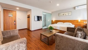 A hotel room with a bed, a TV, a wooden floor, a sofa, a coffee table, and a wall-mounted lamp. - Jinjiang Inn Wuqing Traditional Chinese Medical Hospital Hotel Tianjin (Tianjin)