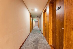 A hotel hallway with carpeted flooring, wooden doors, and a sign indicating room numbers.