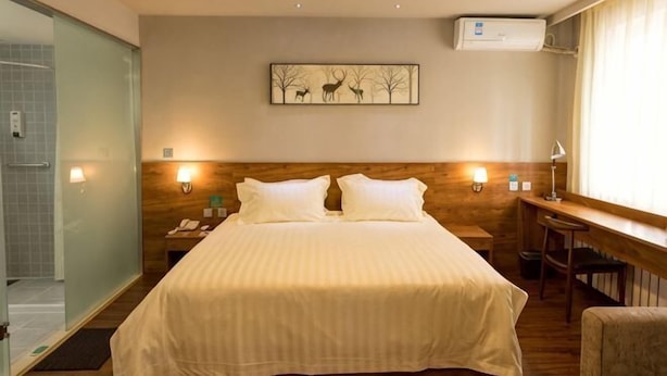 A hotel room with a bed, a desk, a chair, a nightstand, a wall-mounted air conditioner, and a framed picture on the wall. - Jinjiang Inn Wuqing Traditional Chinese Medical Hospital Hotel Tianjin (Tianjin)