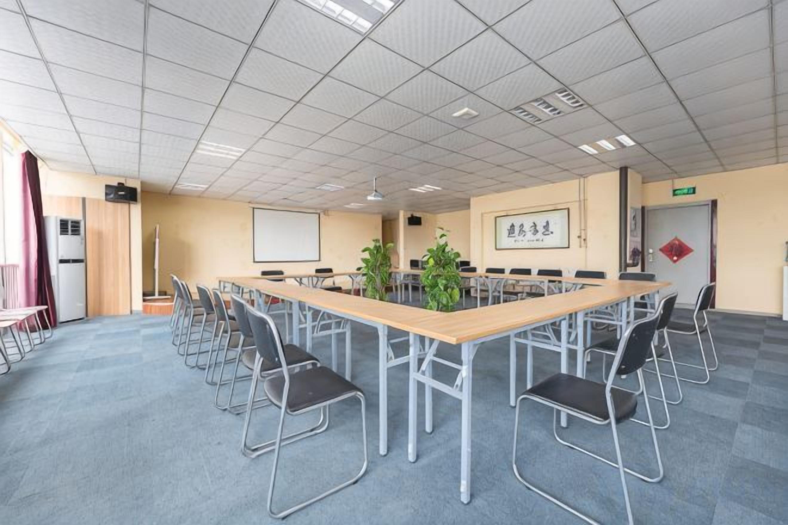 Ein Konferenzraum mit einem langen Tisch, Stühlen, einer Projektionsleinwand und einer Pflanze.