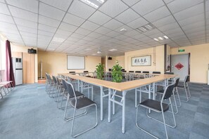 A conference room with a long table, chairs, a projector screen, and a plant.