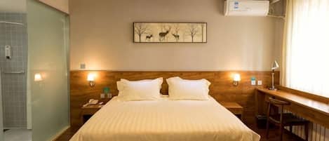 A hotel room with a bed, bedside table, lamp, and a painting on the wall.