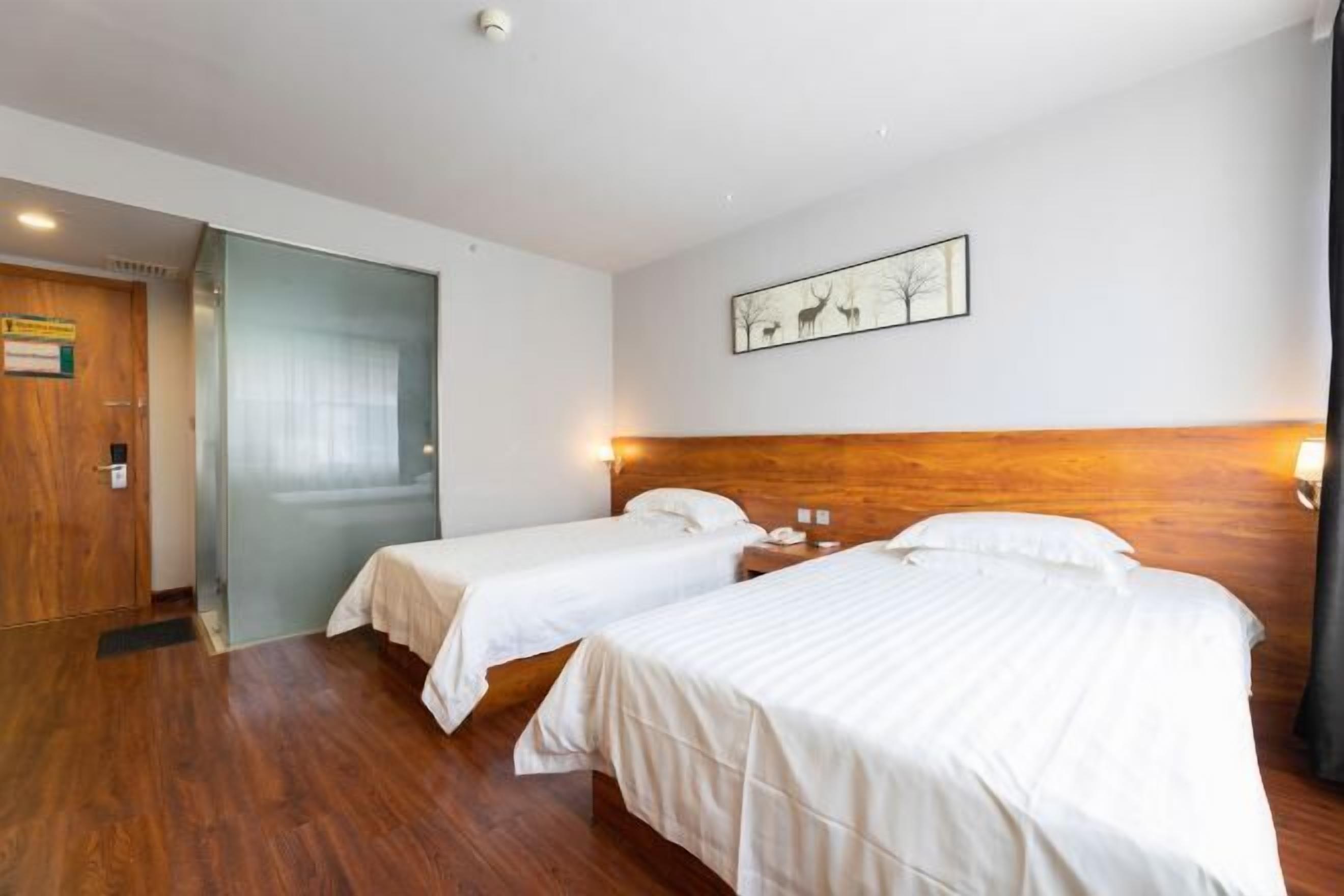 A hotel room with two beds, a wooden headboard, a framed picture on the wall, and a door to the left.