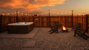 Un patio trasero con jacuzzi, fogata y luces colgantes.