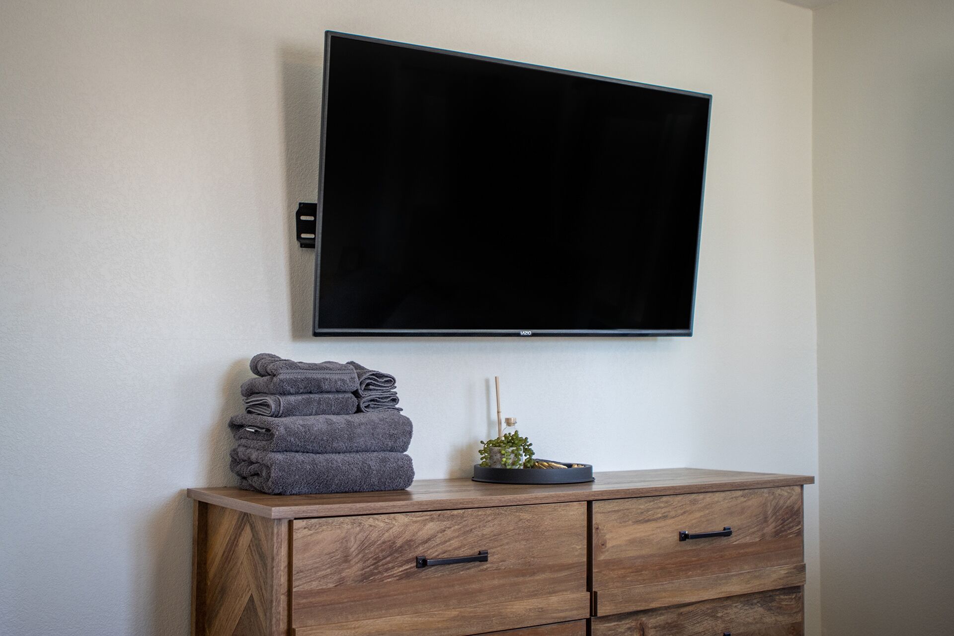 A flat-screen TV mounted on a wall above a wooden dresser with drawers.