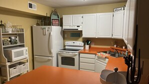 Una cocina con armarios blancos, un refrigerador, un horno, un microondas y un lavamanos.
