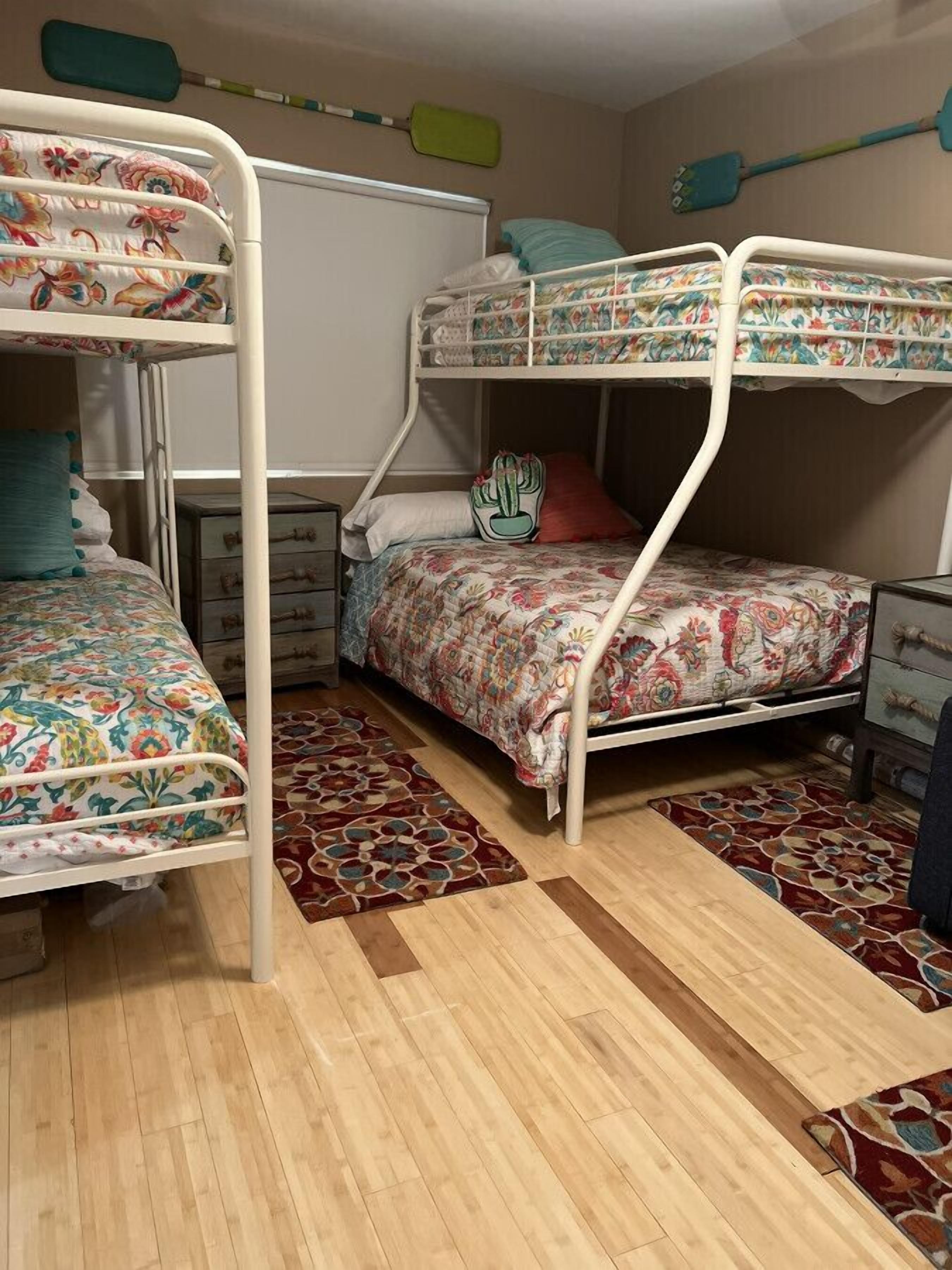Een slaapkamer met stapelbedden, bloemenbeddengoed, een houten vloer en een klein dressoir.
