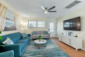A living room with a blue sofa, a grey sofa, a coffee table, a TV, and a ceiling fan.