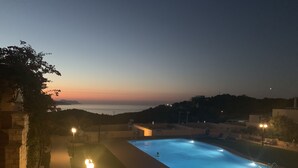 A swimming pool at dusk with a view of the sea and distant hills.