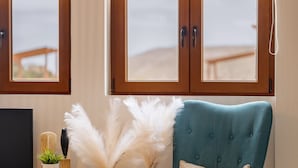 A modern living room with a teal armchair, a wooden cabinet, a TV, and a large window with a view.