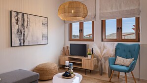 A modern living room with a sofa, a coffee table with decorative items, a television on a wooden cabinet, and a blue armchair.
