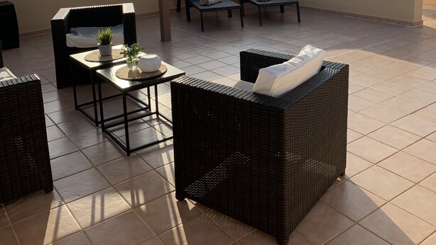 A covered outdoor seating area with wicker furniture and a view of distant mountains.