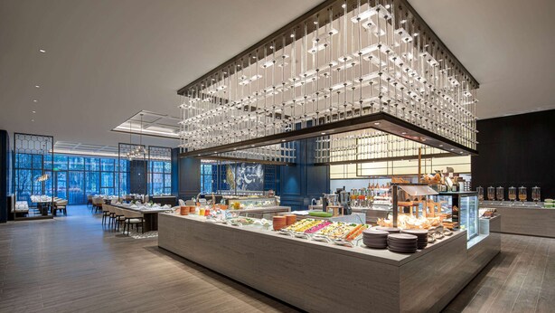A modern breakfast buffet with a central island, glass display cases, and a contemporary light fixture. - Wyndham Changzhou Xinbei (Changzhou)