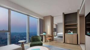 A modern hotel room with a large window offering a city view, a cozy seating area, a small round table, and a built-in wardrobe. - Wyndham Changzhou Xinbei (Changzhou)