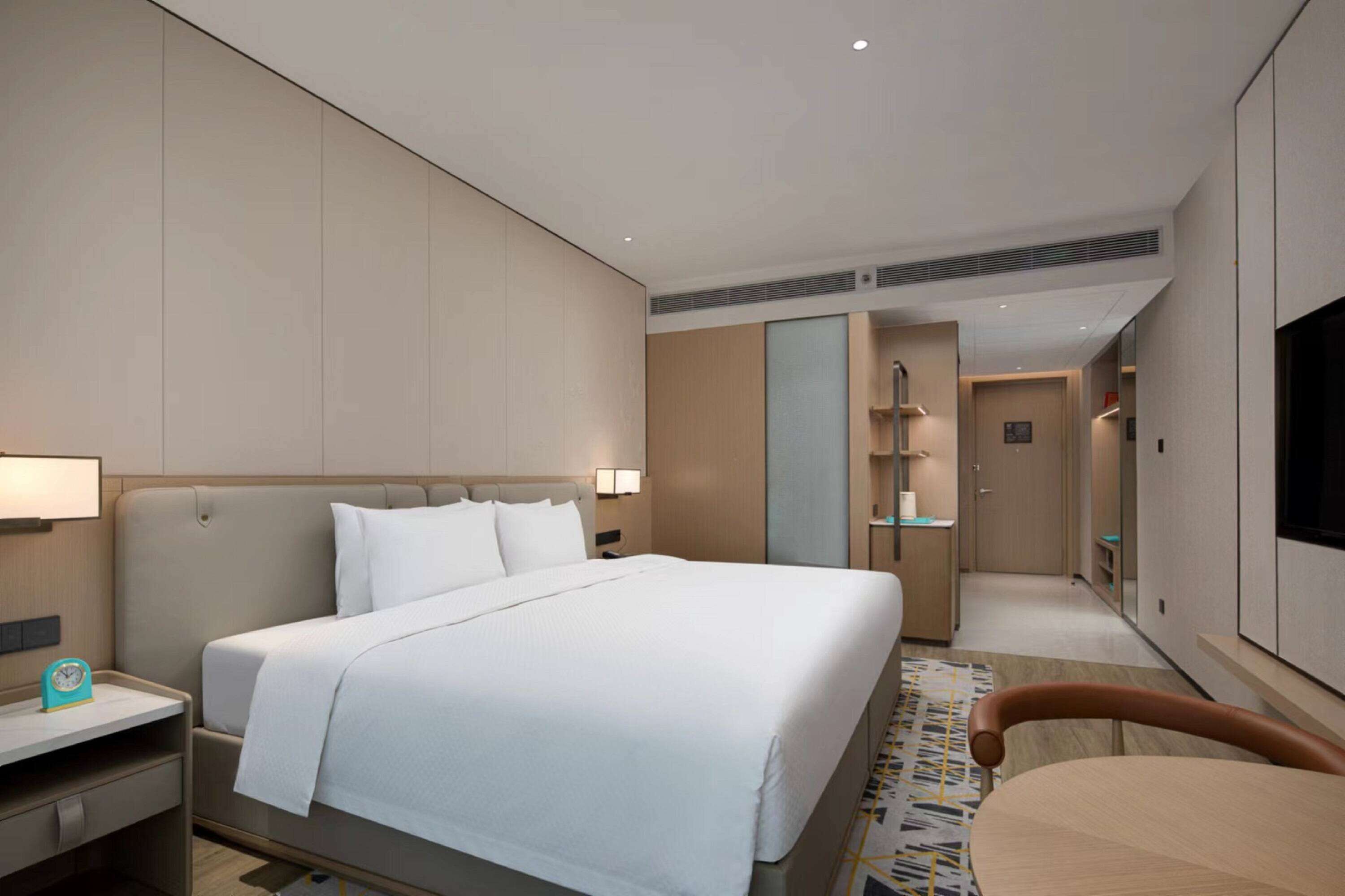 A modern hotel room with a large bed, bedside tables, a TV, and a walk-in closet.