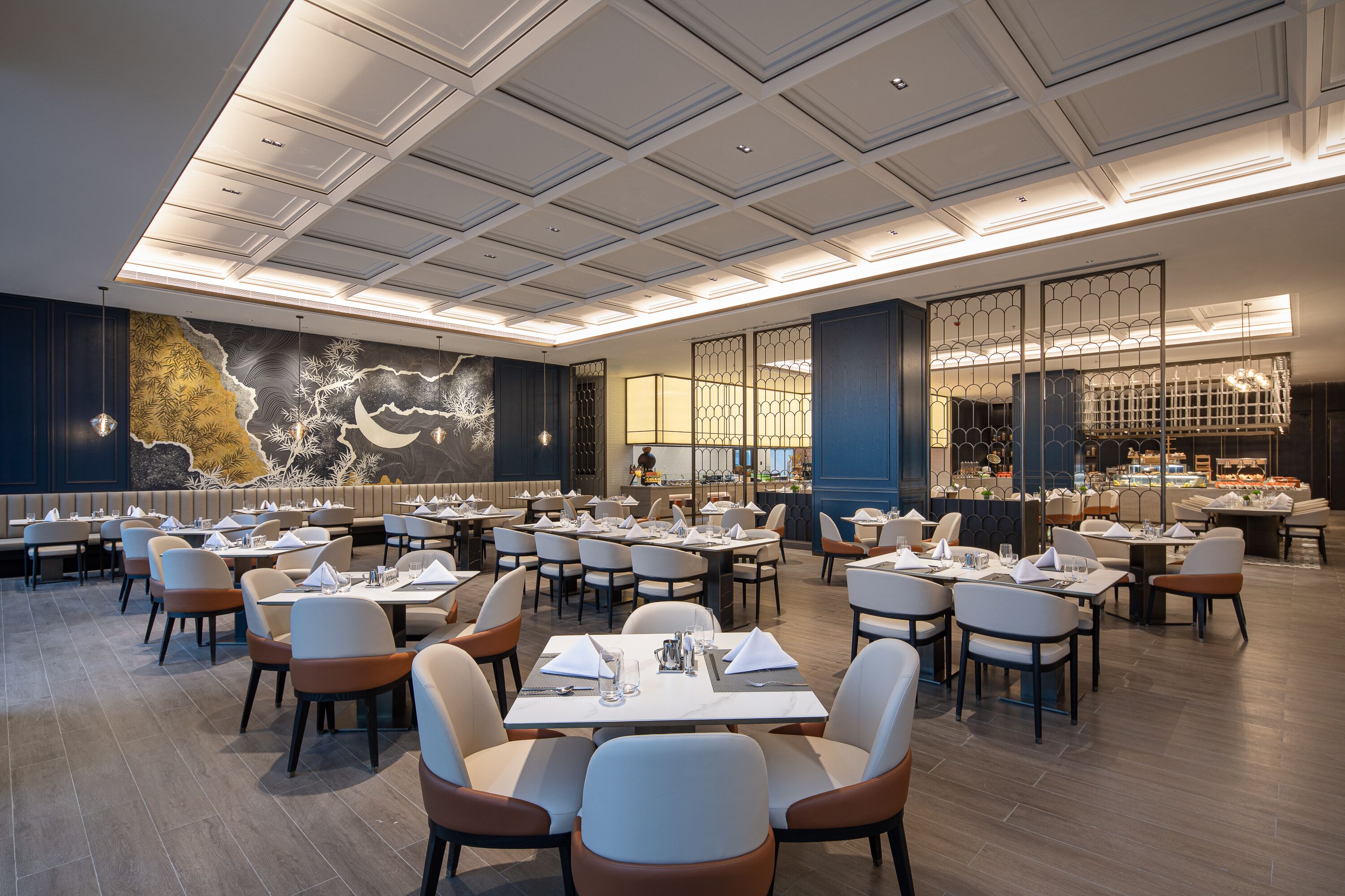 Un restaurant spacieux, doté de nombreuses tables et chaises, d’une fresque murale décorative et d’un plafond bien éclairé.