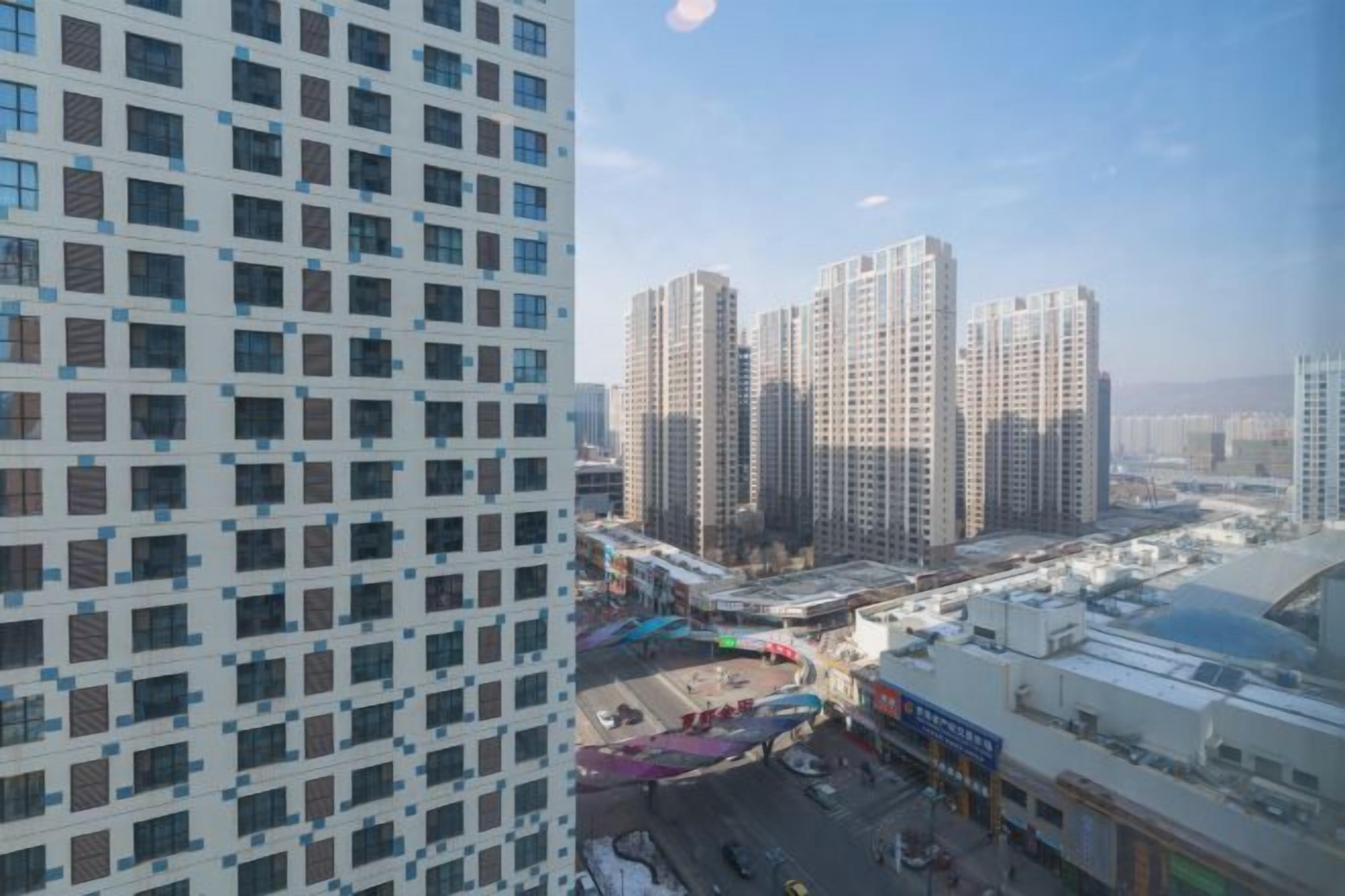 A high-rise building with a grid-like facade, a commercial area with shops, and a clear sky.