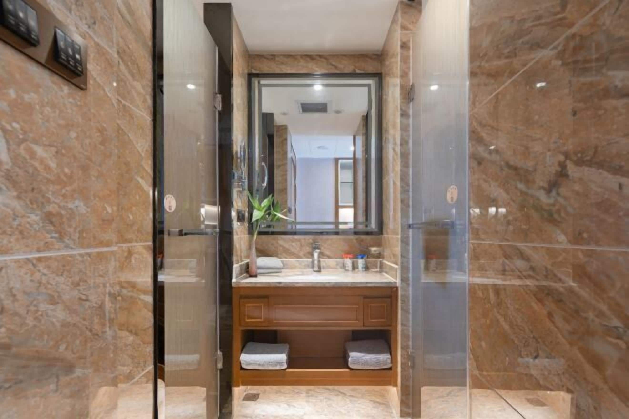 A modern bathroom with a marble wall, a glass-enclosed shower, a wooden vanity, and a large mirror.