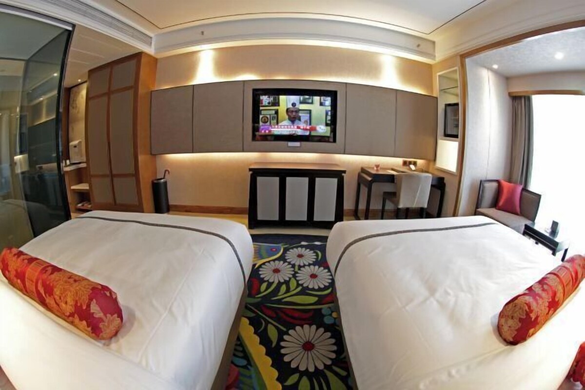 A hotel room with two beds, a TV mounted on the wall, a small desk, and a chair.