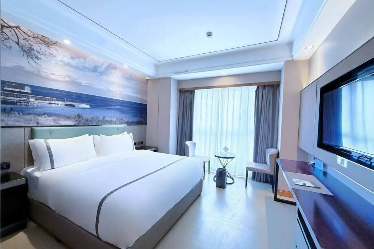 A modern hotel room with a large bed, a TV, a desk, and a view of the ocean.
