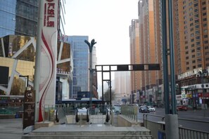 Une rue moderne en milieu urbain, bordée d’immeubles imposants, avec un passage piéton et un arrêt de bus.