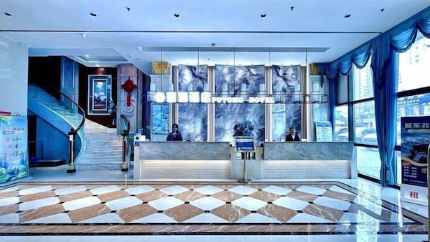 Un hall d’hôtel moderne avec un comptoir d’accueil, un escalier et de grandes fenêtres.