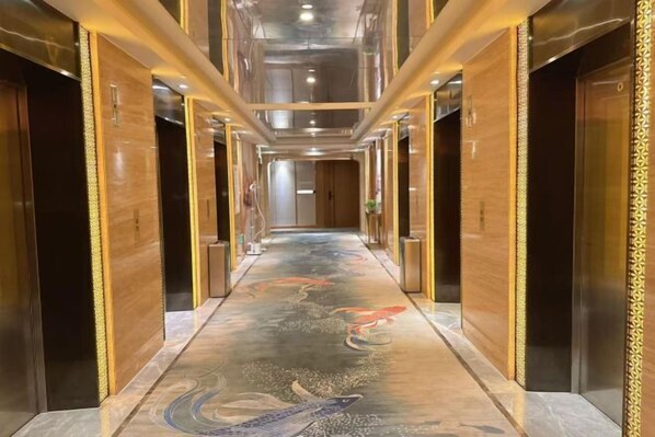 A hallway with a long, narrow corridor, flanked by wooden doors and walls, leading to an elevator area. - Putong Hotel (Xining)