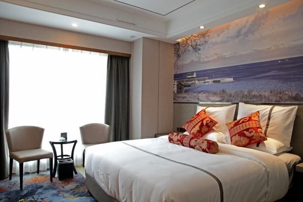 A hotel room with a large bed, two chairs, a small table, and a painting on the wall.